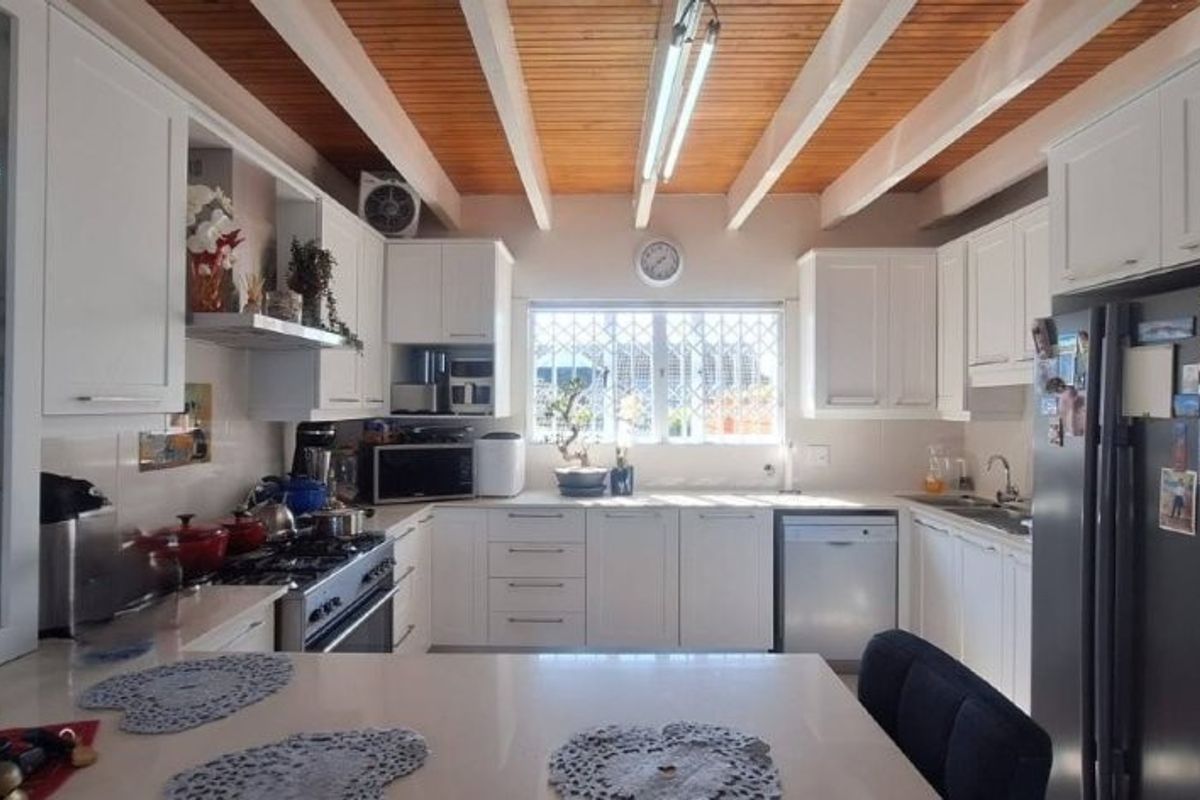 A well-lit kitchen featuring white cabinetry, stone countertops, a gas stove, and a distinctive exposed timber beam ceiling.