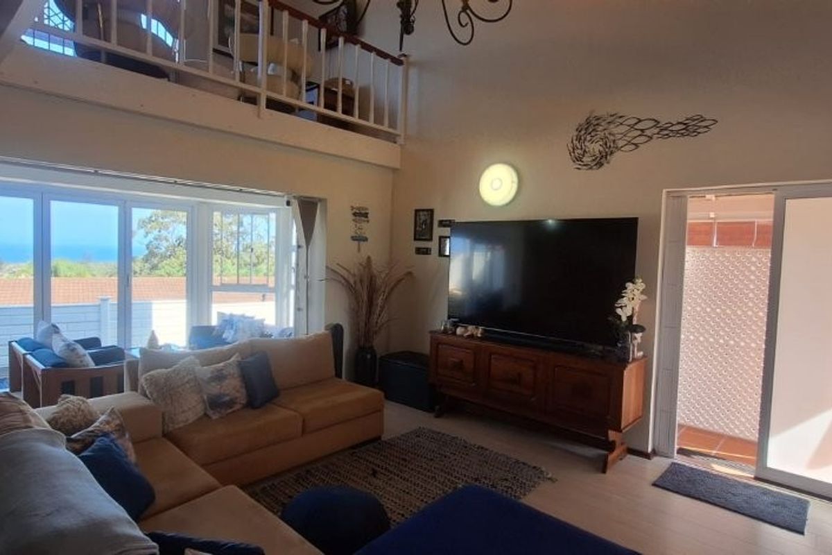 Spacious living room featuring a mezzanine level, large sliding glass doors with ocean views, and timber flooring, creating a bright and airy atmosphere.