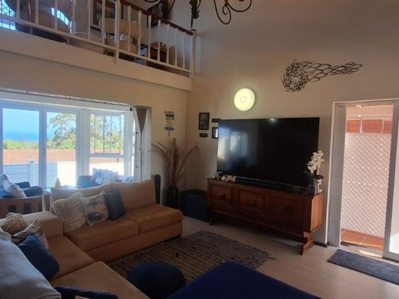 Spacious living room featuring a mezzanine level, large sliding glass doors with ocean views, and timber flooring, creating a bright and airy atmosphere.