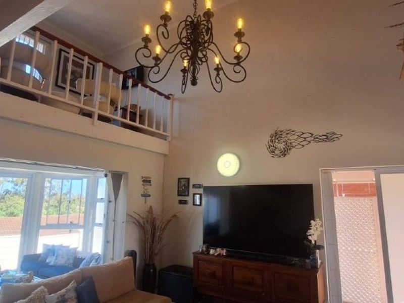 Spacious open-plan living area featuring a mezzanine level, exposed timber beams, a decorative chandelier, and large sliding doors offering scenic views.