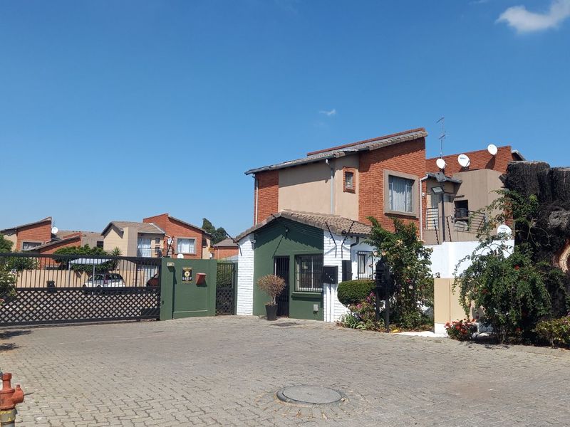 Front entrance view of the apartment complex featuring a paved driveway, security gate, and guard house structure.