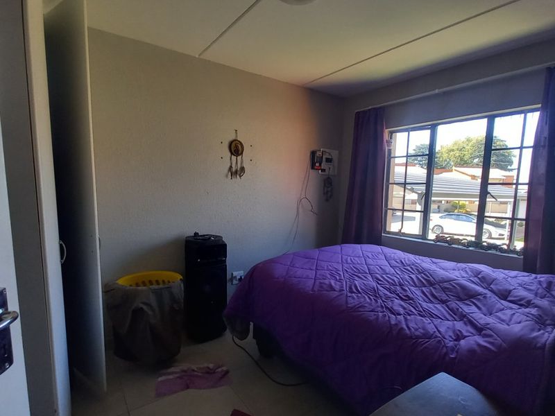 A functional bedroom featuring tiled flooring, a built-in cupboard, and a window with security bars, offering a practical living space.