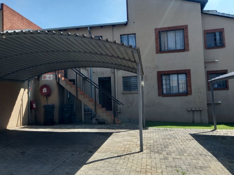Exterior view of an apartment complex featuring a covered carport, paved driveway, and an external staircase leading to upper levels.