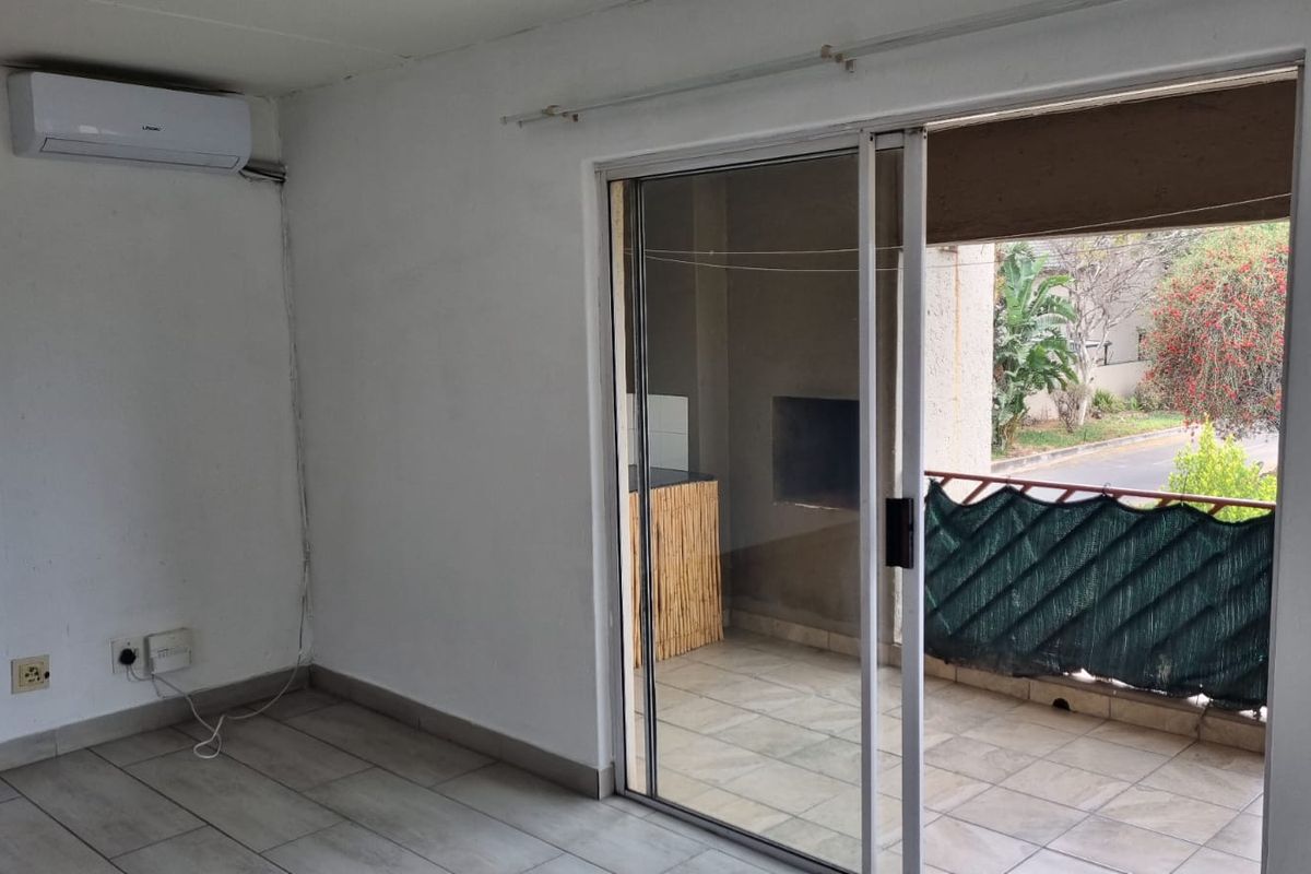 An empty living room featuring tiled flooring, a wall-mounted air conditioning unit, and a sliding glass door leading to an outdoor balcony area.