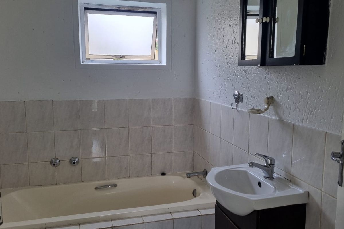 A functional bathroom featuring a built-in bathtub, a vanity basin with storage, and tiled splashbacks, requiring cosmetic updates to modernize the space.