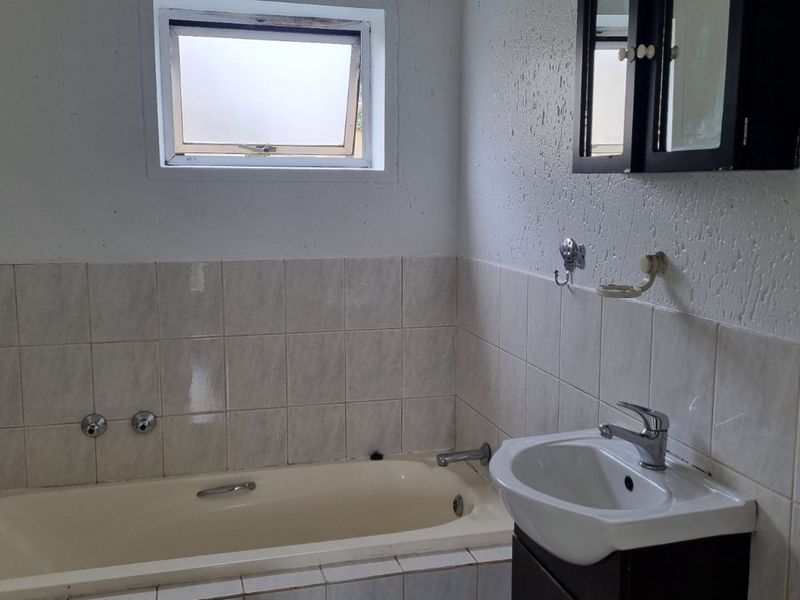 A functional bathroom featuring a built-in bathtub, a vanity basin with storage, and tiled splashbacks, requiring cosmetic updates to modernize the space.