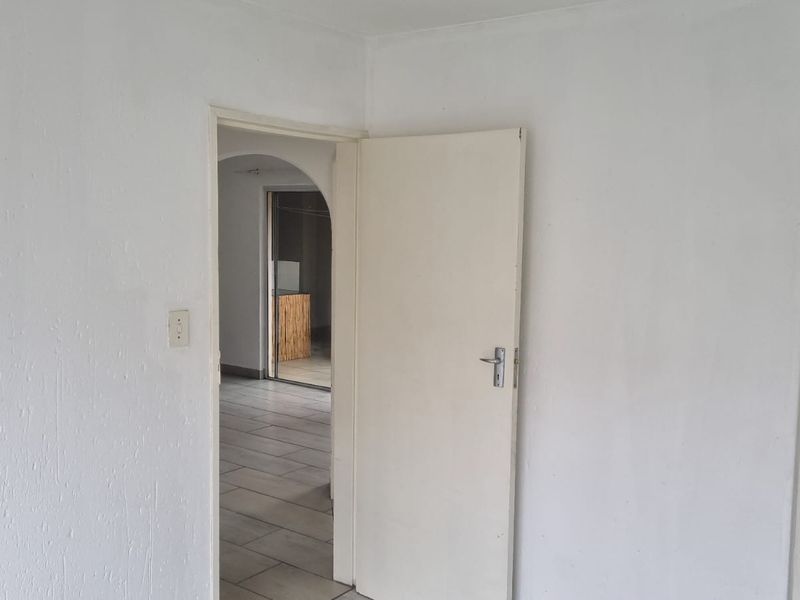 An empty hallway featuring tiled flooring and a white internal door, leading into an adjacent room with an arched entryway.