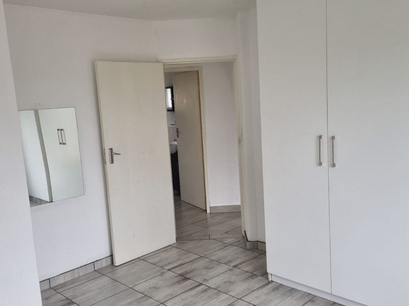 A vacant bedroom featuring tiled flooring and built-in cupboards, with a doorway leading to an adjacent bathroom area.