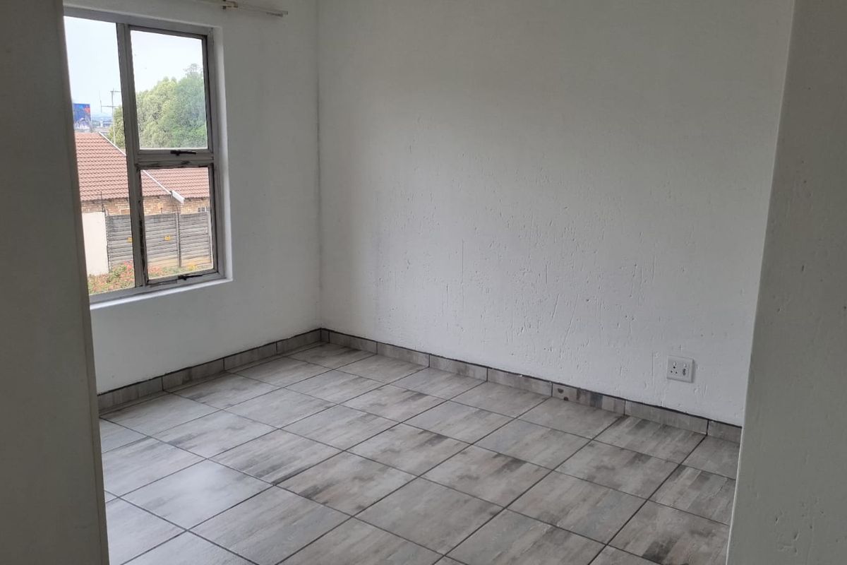An empty bedroom featuring neutral tiled flooring and a single aluminium-framed window, providing a blank canvas for personalization.