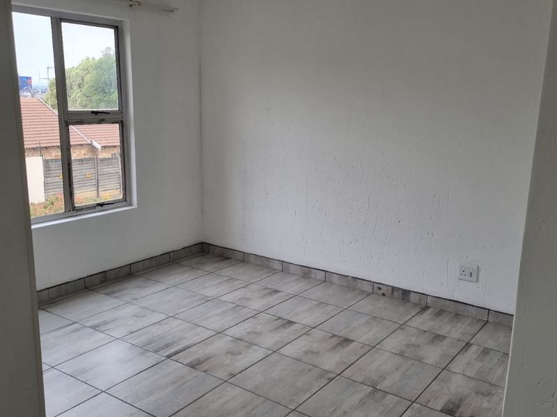 An empty bedroom featuring neutral tiled flooring and a single aluminium-framed window, providing a blank canvas for personalization.