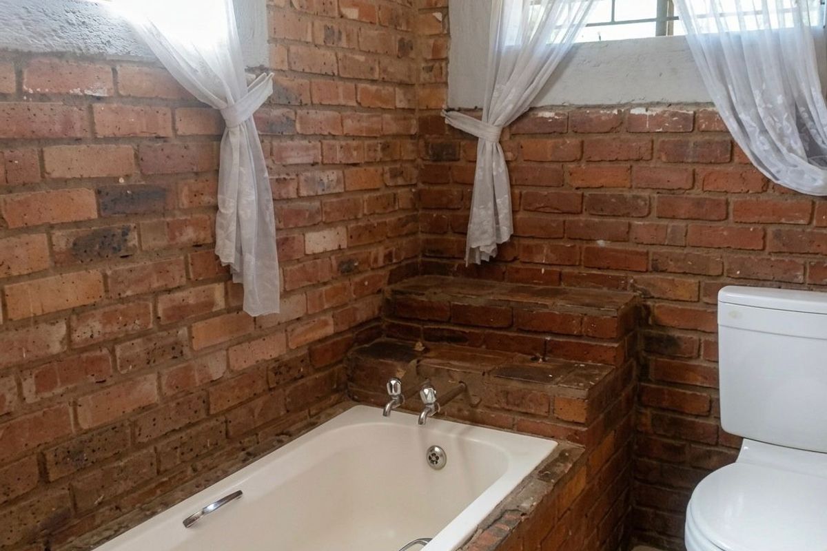 Bathroom featuring exposed brick walls, a built-in brick-surround bathtub, and a standard toilet, offering a rustic aesthetic in need of cosmetic updates.