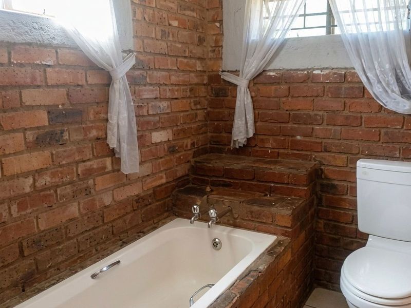 Bathroom featuring exposed brick walls, a built-in brick-surround bathtub, and a standard toilet, offering a rustic aesthetic in need of cosmetic updates.