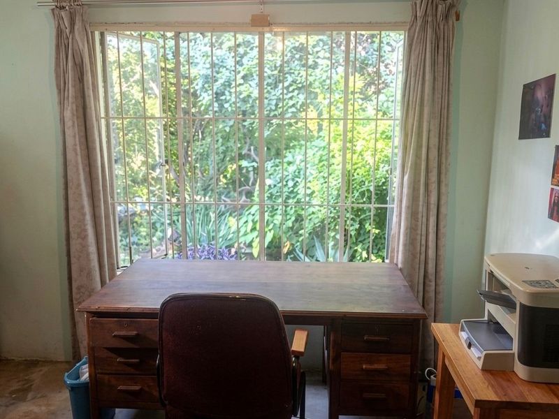 A functional home office space featuring a large window with security bars, overlooking a lush garden area.
