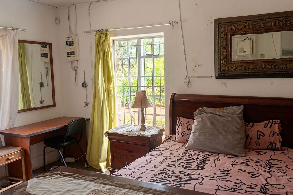 A bedroom featuring security bars on the window and exposed electrical conduit, requiring cosmetic updates to improve the overall finish and aesthetic appeal.