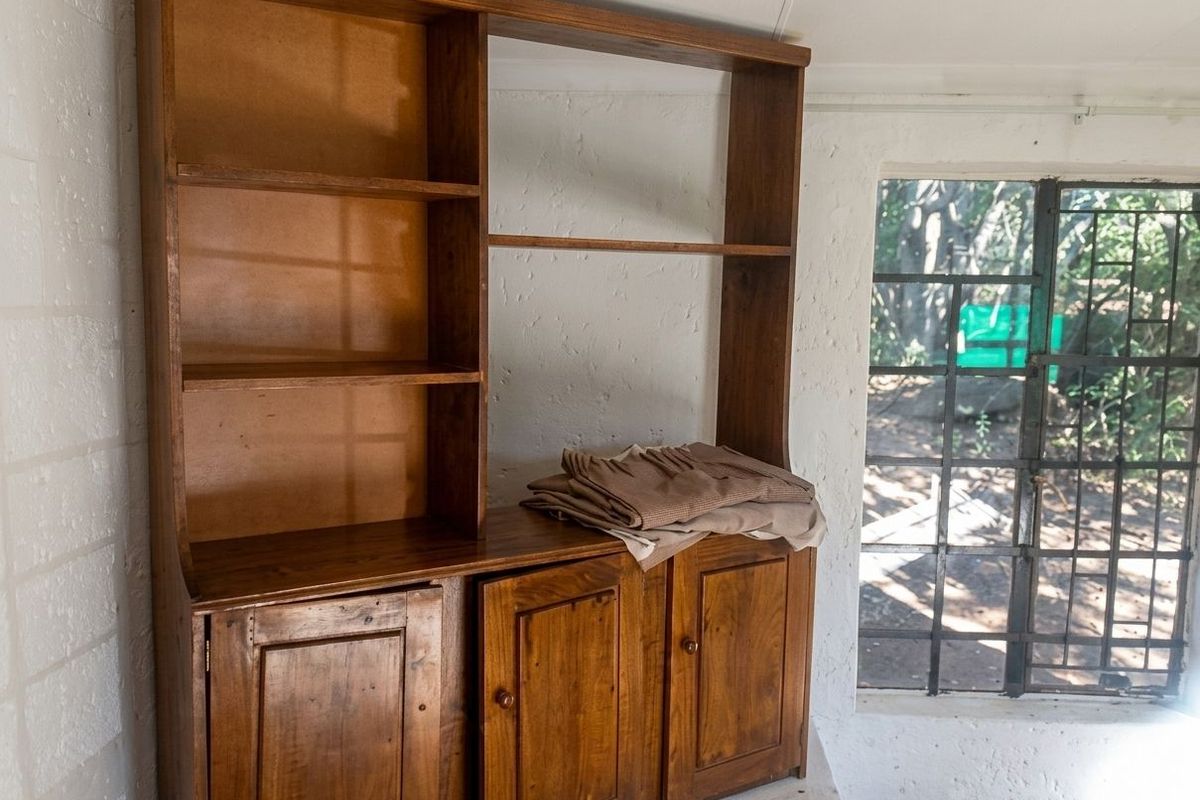 A small interior space featuring a built-in wooden storage unit and a window with a metal security grille.