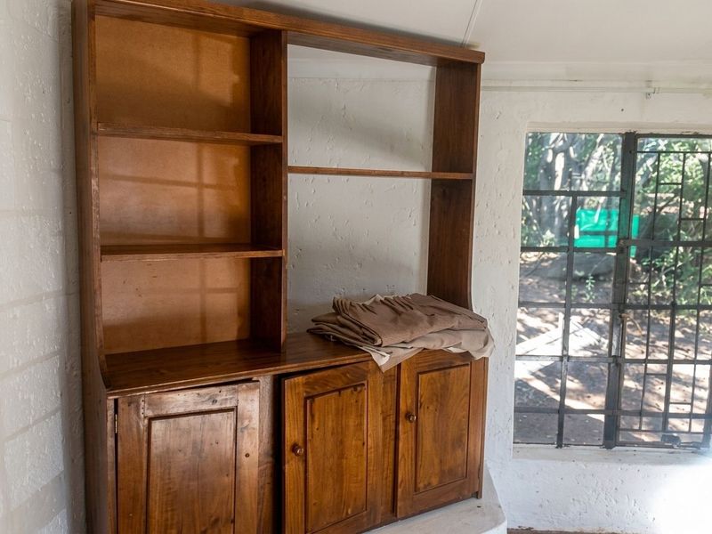 A small interior space featuring a built-in wooden storage unit and a window with a metal security grille.