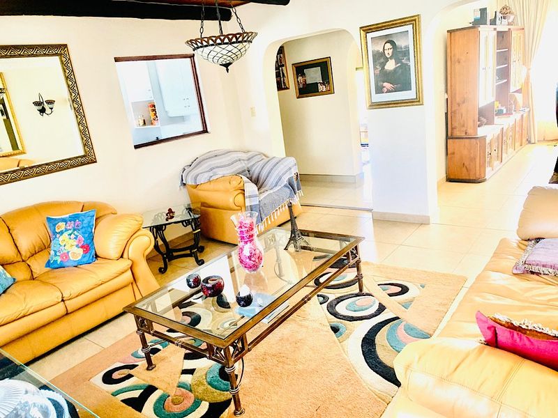 A living room featuring tiled flooring, exposed ceiling beams, and an arched entryway leading to adjacent living spaces.