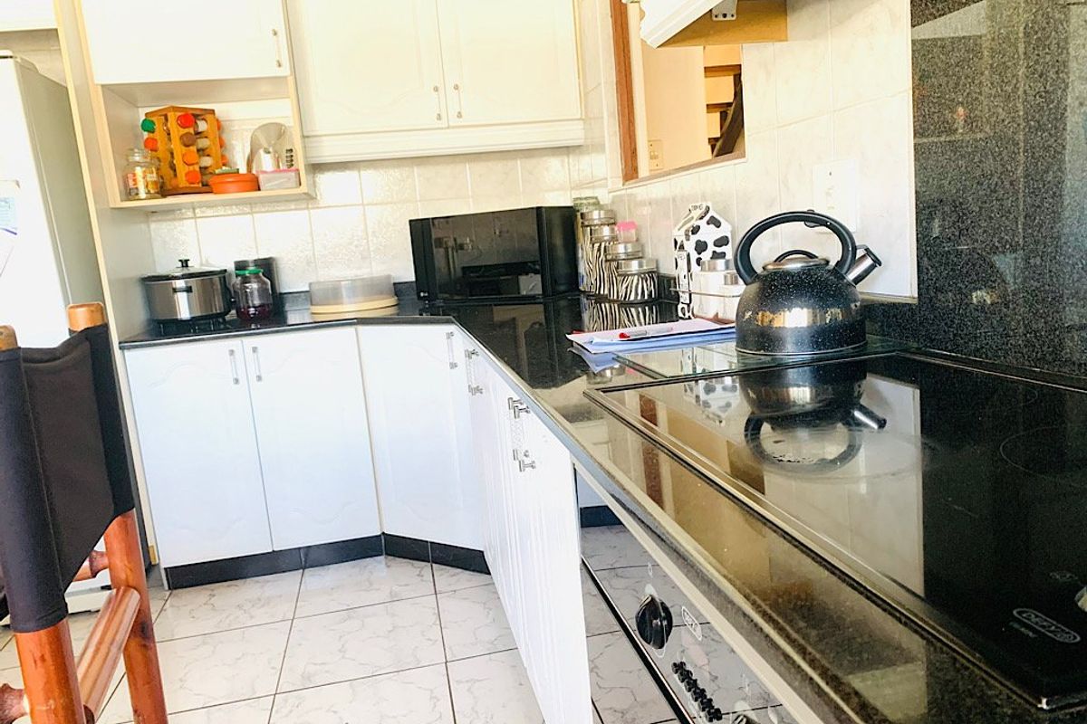 A functional kitchen featuring white cabinetry, black granite countertops, ceramic tile flooring, and integrated cooking appliances.