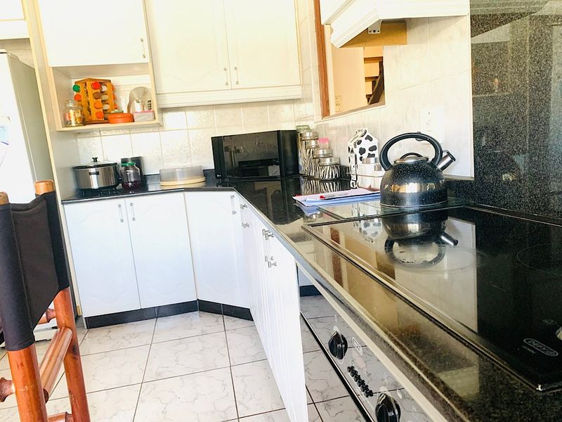 A functional kitchen featuring white cabinetry, black granite countertops, ceramic tile flooring, and integrated cooking appliances.