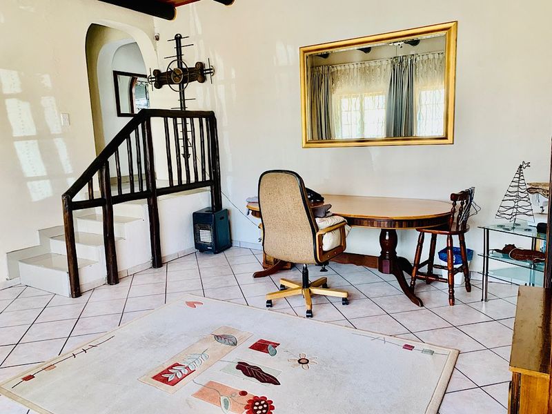 A living area featuring tiled flooring, an arched entryway, and a wooden staircase with a traditional balustrade.