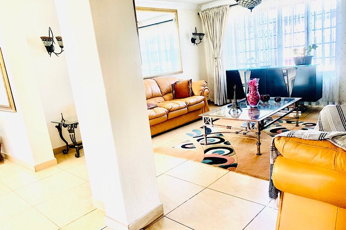 A bright living room featuring tiled flooring, decorative wall sconces, and a large window allowing for ample natural light.