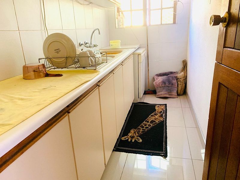 A functional scullery area featuring built-in cabinetry, a stainless steel sink, and tiled splashbacks, offering practical utility space for food preparation and cleaning.