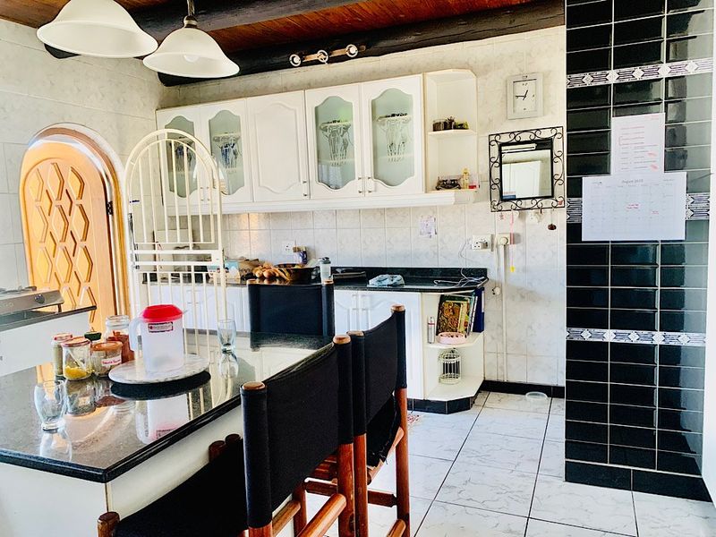 A functional kitchen featuring granite countertops, white cabinetry, and exposed timber ceiling beams, with a distinct tiled backsplash and arched doorway access.