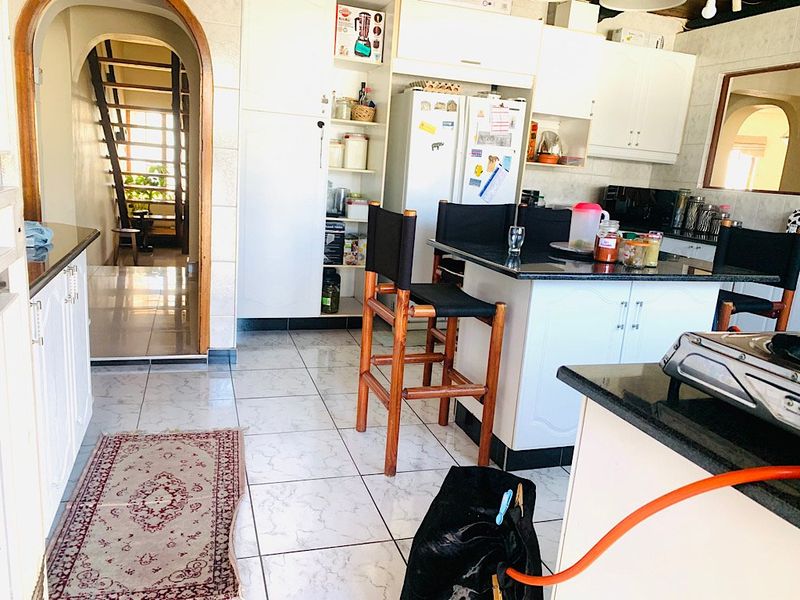 A functional kitchen featuring white cabinetry, dark granite countertops, and tiled flooring, with an adjacent archway leading to a staircase.