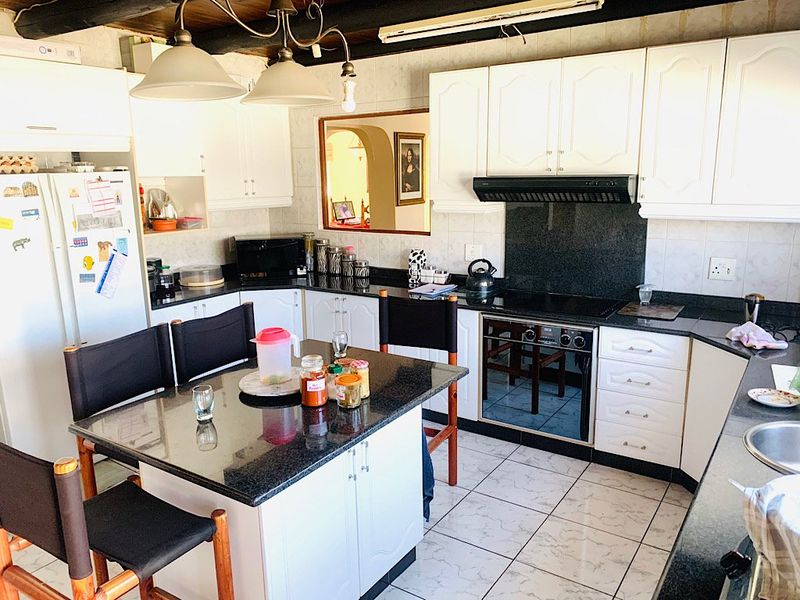A functional kitchen featuring granite countertops, built-in oven, extractor fan, and exposed timber ceiling beams, offering a classic layout with ample storage space.
