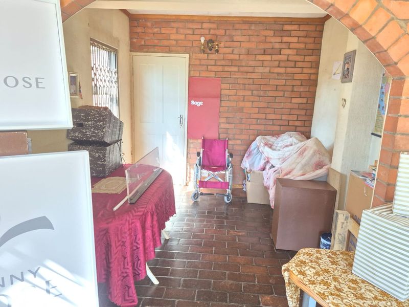 A covered patio area featuring exposed brick walls and tiled flooring, accessible through an arched entryway with a security gate.