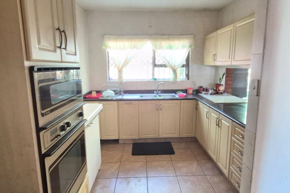 A functional kitchen featuring built-in cabinetry, integrated oven and microwave, double sink, and tiled flooring, offering a dated layout ready for modernization.