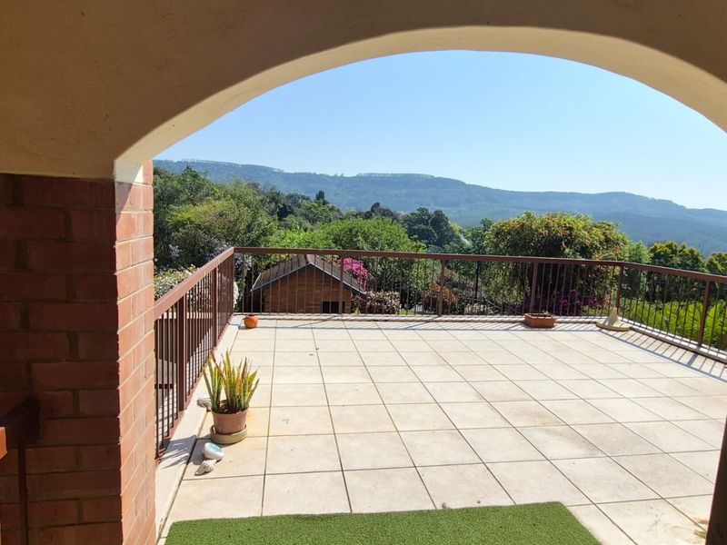 A spacious open-air balcony featuring tiled flooring, a metal balustrade, and a brick archway, offering scenic mountain views.