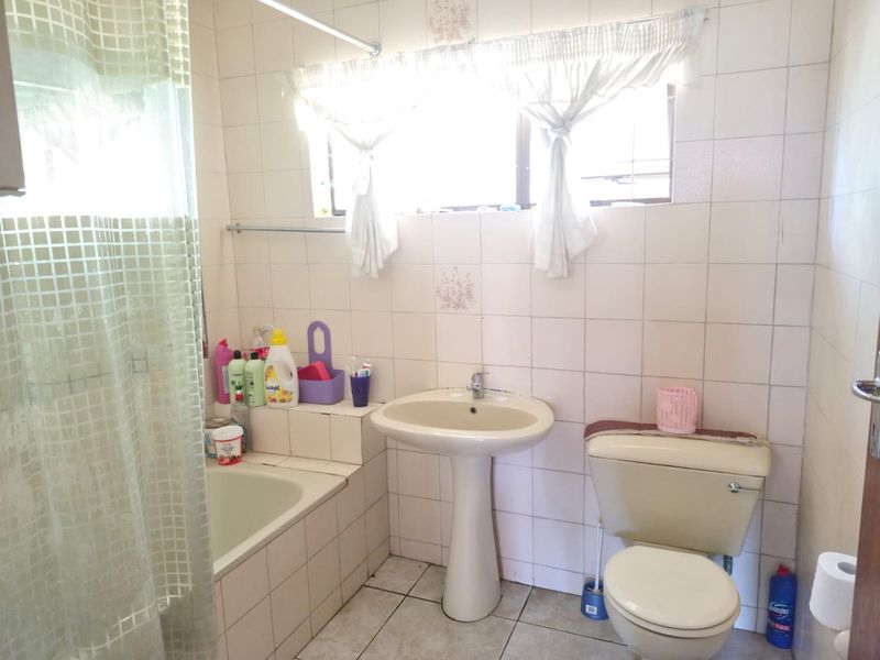 A dated bathroom featuring a pedestal basin, toilet, and built-in bathtub with full-height wall tiling and tiled flooring.