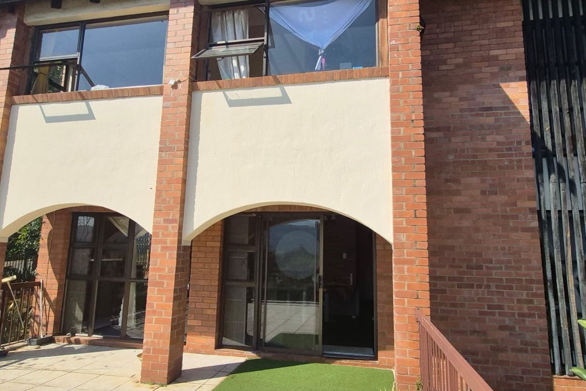 Rear exterior view of a two-story brick house featuring arched masonry details, a tiled patio area, and large sliding glass doors.