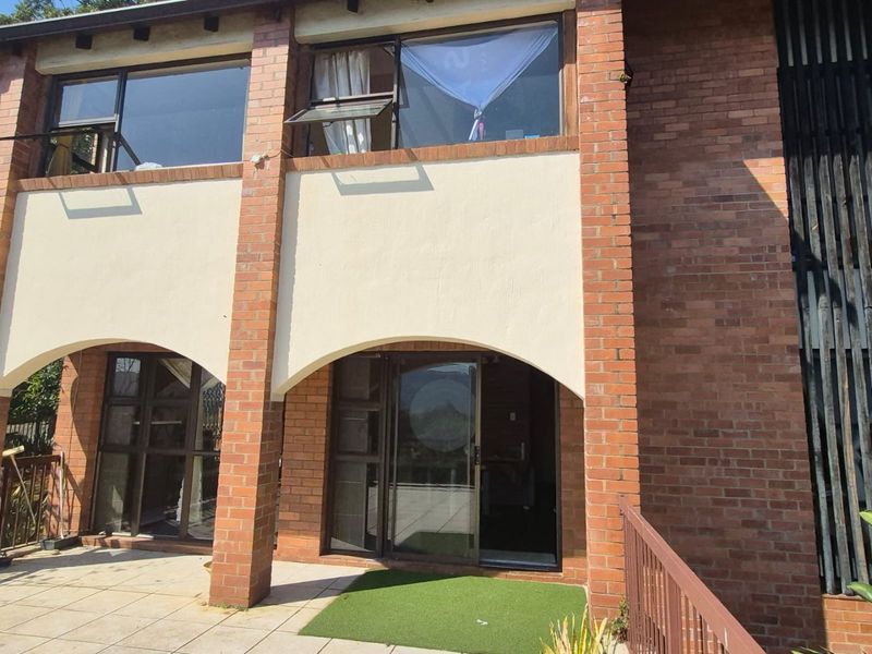 Rear exterior view of a two-story brick house featuring arched masonry details, a tiled patio area, and large sliding glass doors.