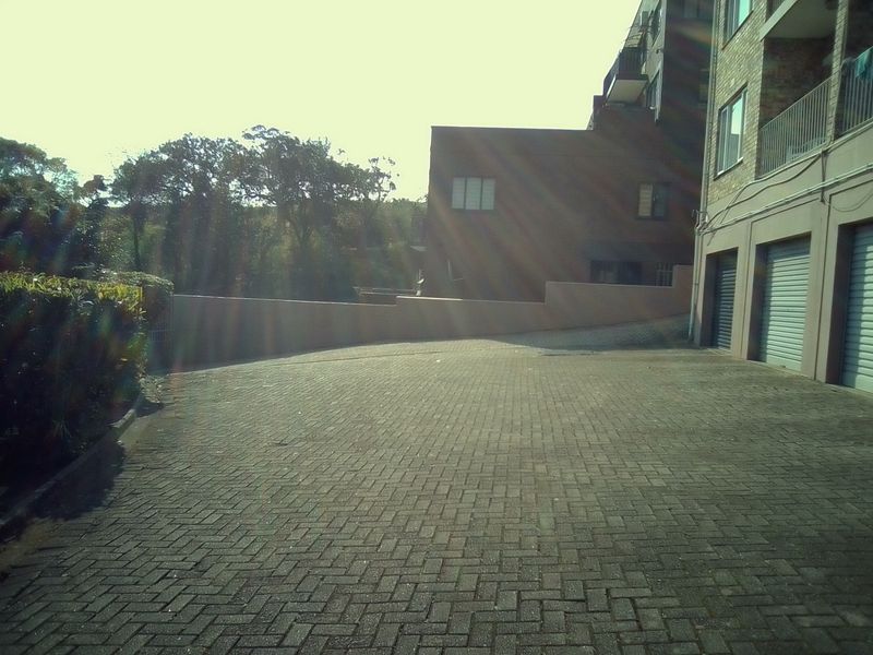 Exterior view of the apartment complex featuring a paved driveway, retaining wall, and multiple garage access points.