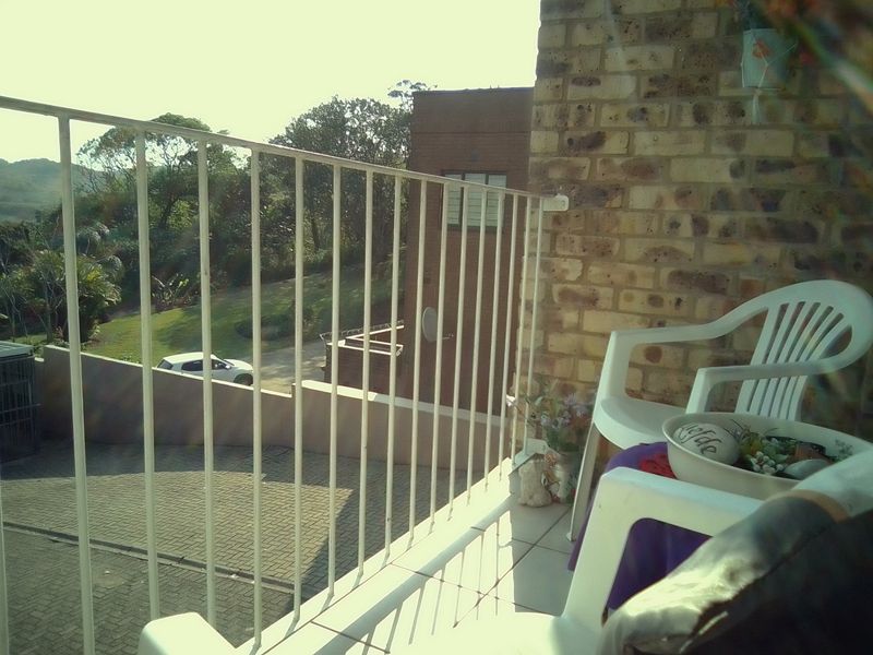 A balcony featuring a metal balustrade, exposed brick wall, and tiled flooring, overlooking the surrounding neighborhood and driveway area.