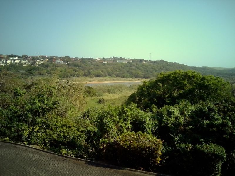 A scenic elevated view overlooking a lush green valley, natural landscape, and distant residential neighborhood.