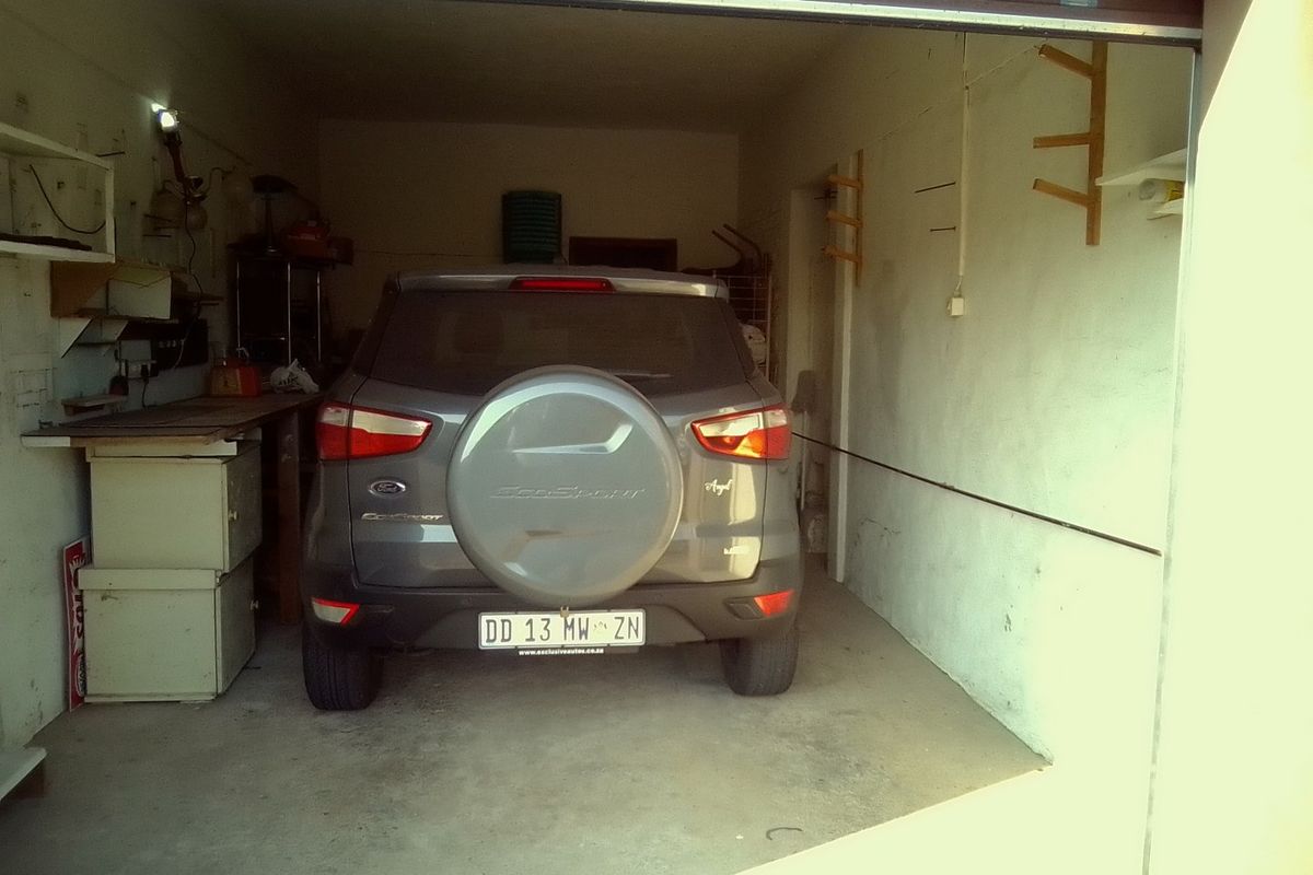 A functional single-car garage featuring concrete flooring, wall-mounted storage racks, and a roll-up garage door.