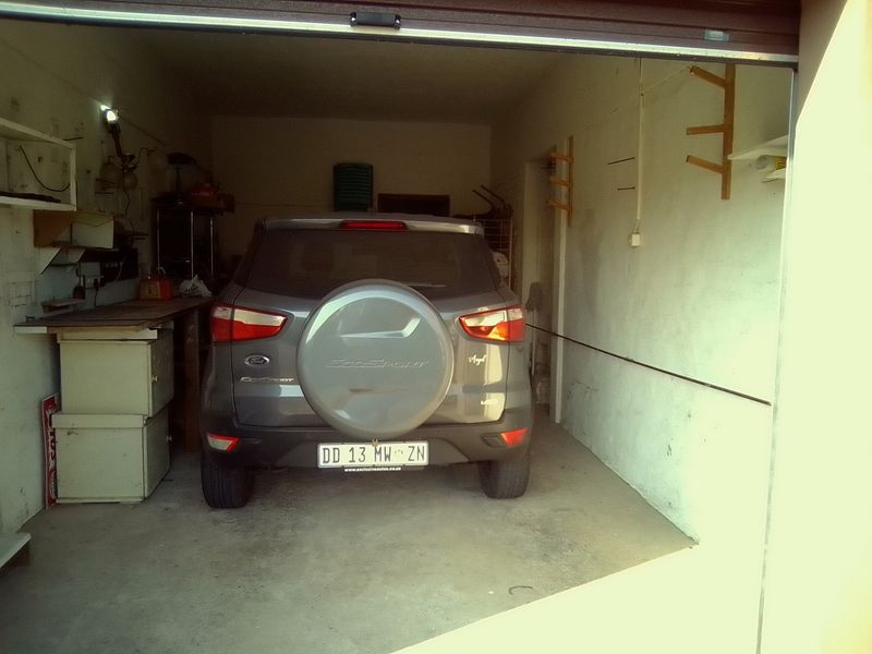 A functional single-car garage featuring concrete flooring, wall-mounted storage racks, and a roll-up garage door.
