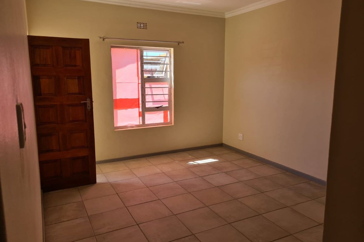 A vacant bedroom featuring neutral wall paint, tiled flooring, and a wooden door, offering a clean and versatile space ready for personalization.