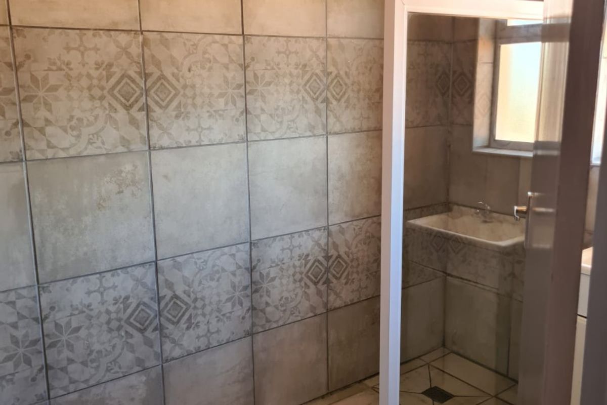 A bathroom featuring tiled walls and flooring with a walk-in shower enclosure, currently requiring finishing touches to the shower door and trim.
