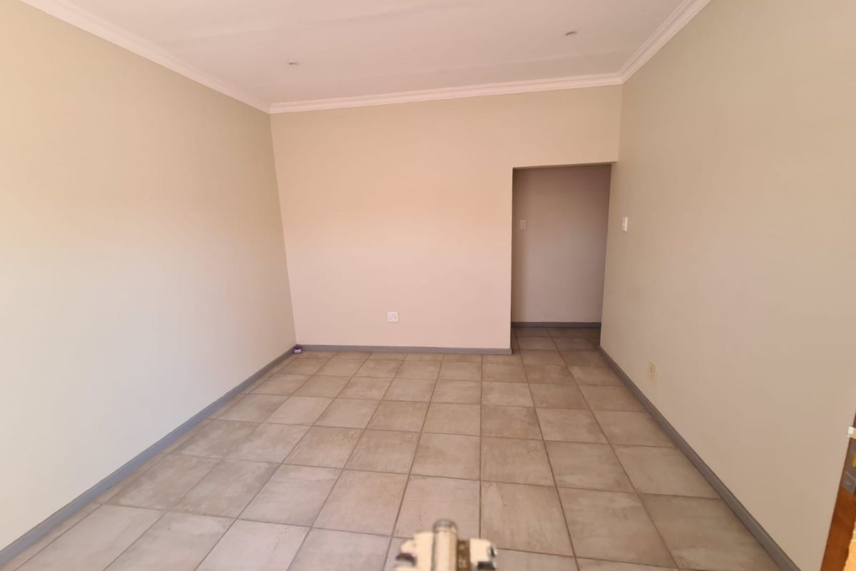 An empty, neutral-toned living area featuring ceramic floor tiles, coved ceilings, and recessed lighting, offering a blank canvas for interior design.