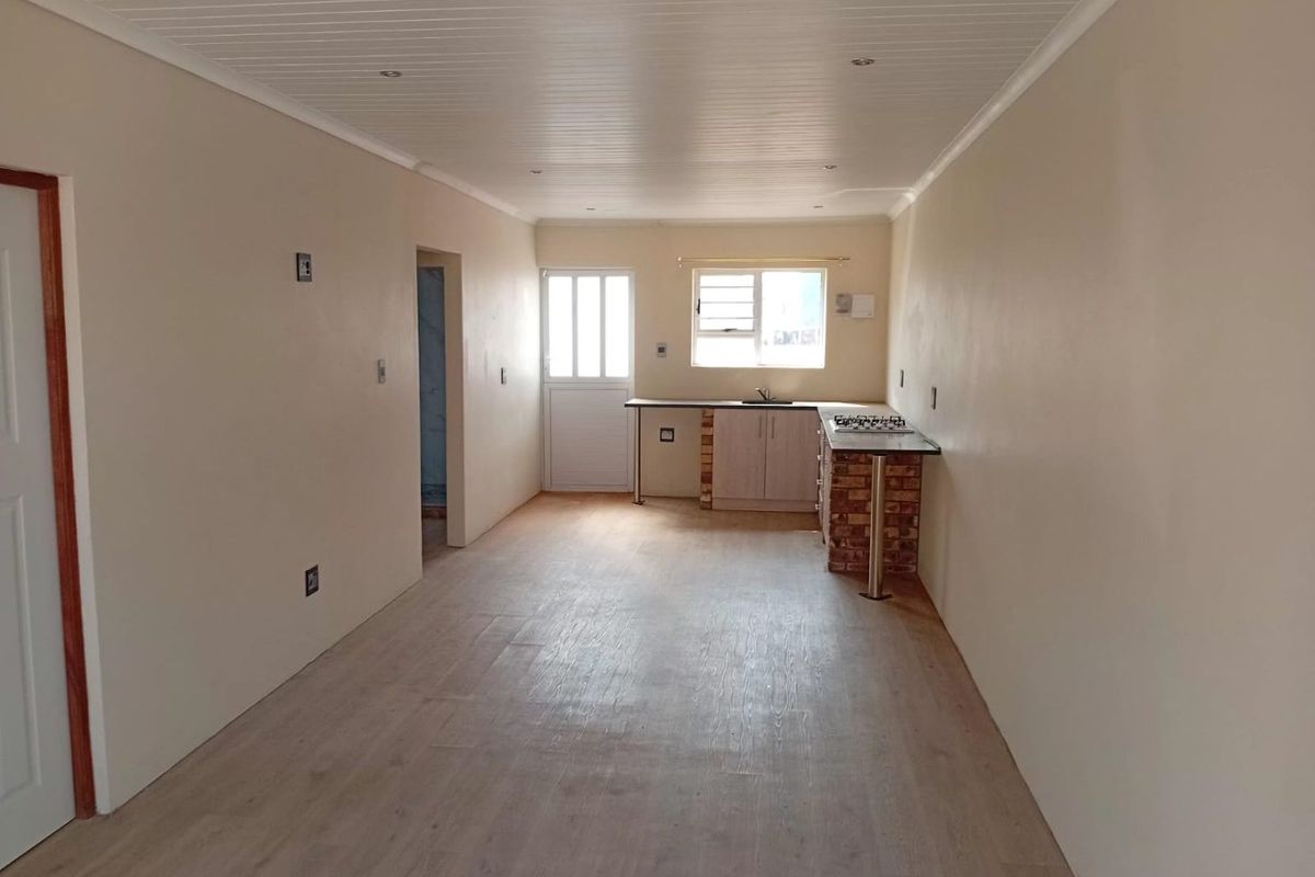 An open-plan living and kitchen area featuring laminate flooring, a tongue and groove ceiling, and a compact kitchen with a built-in hob.