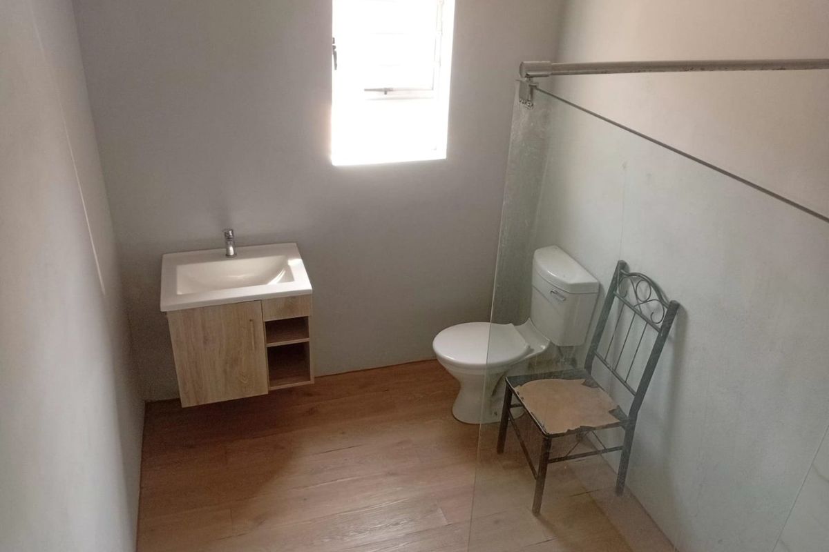 A clean, modern bathroom featuring a wall-mounted vanity, a standard toilet, and a glass shower screen with light wood-look flooring.