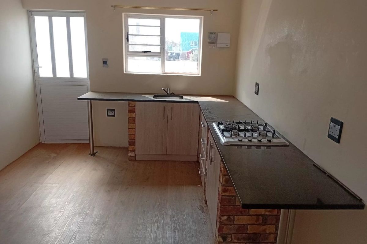 A functional kitchen featuring built-in cabinetry, a gas hob, stone countertops, and exposed brick supports, with direct access to an exterior door.