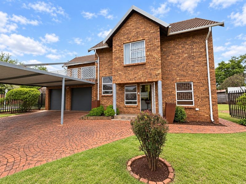A double-storey face brick house featuring a paved driveway, double garage, attached carport, and an upper-level balcony.