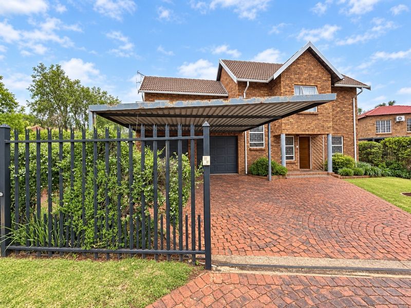 Front view of a double-story brick house featuring a paved driveway, integrated garage, and a metal carport structure.