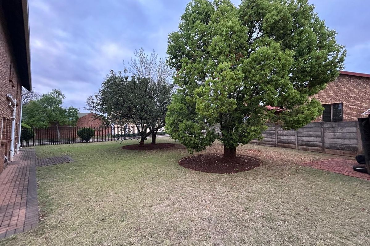 A spacious rear garden featuring a paved walkway, mature trees, and secure perimeter fencing, providing a private outdoor area.