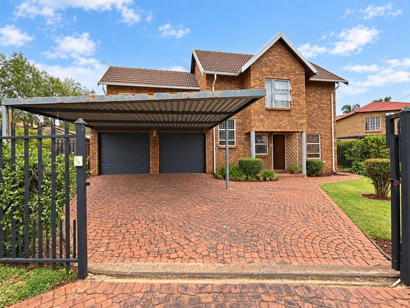 Front view of a double-story brick house featuring a paved driveway, double garage, and a covered carport with a secure gated entrance.